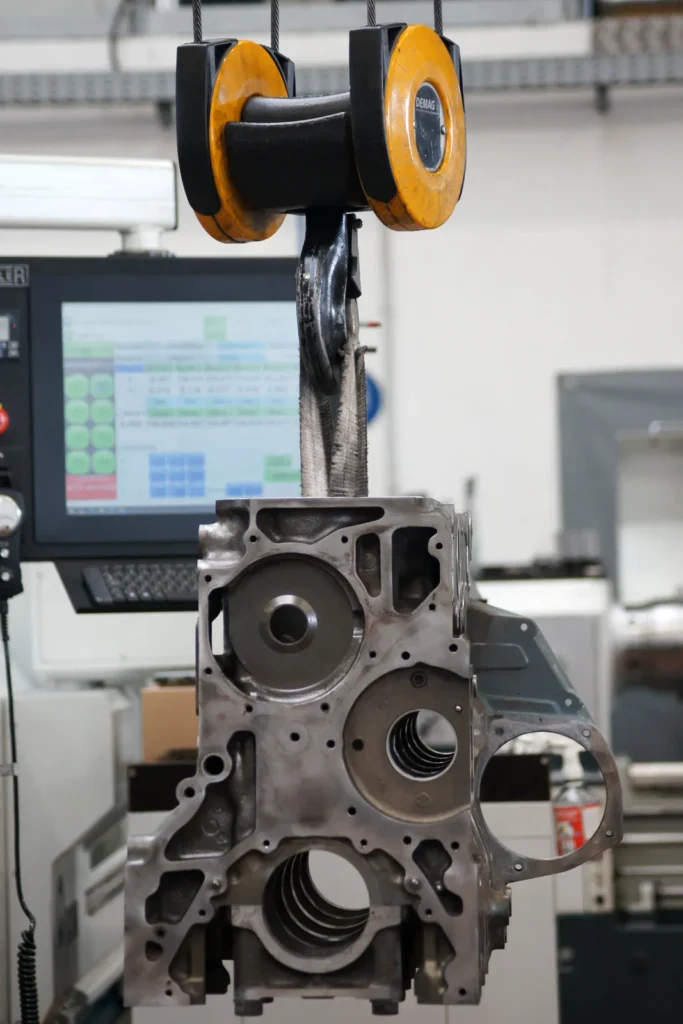 Motorblock hängt am Kran vor einer CNC-Bearbeitungsmaschine